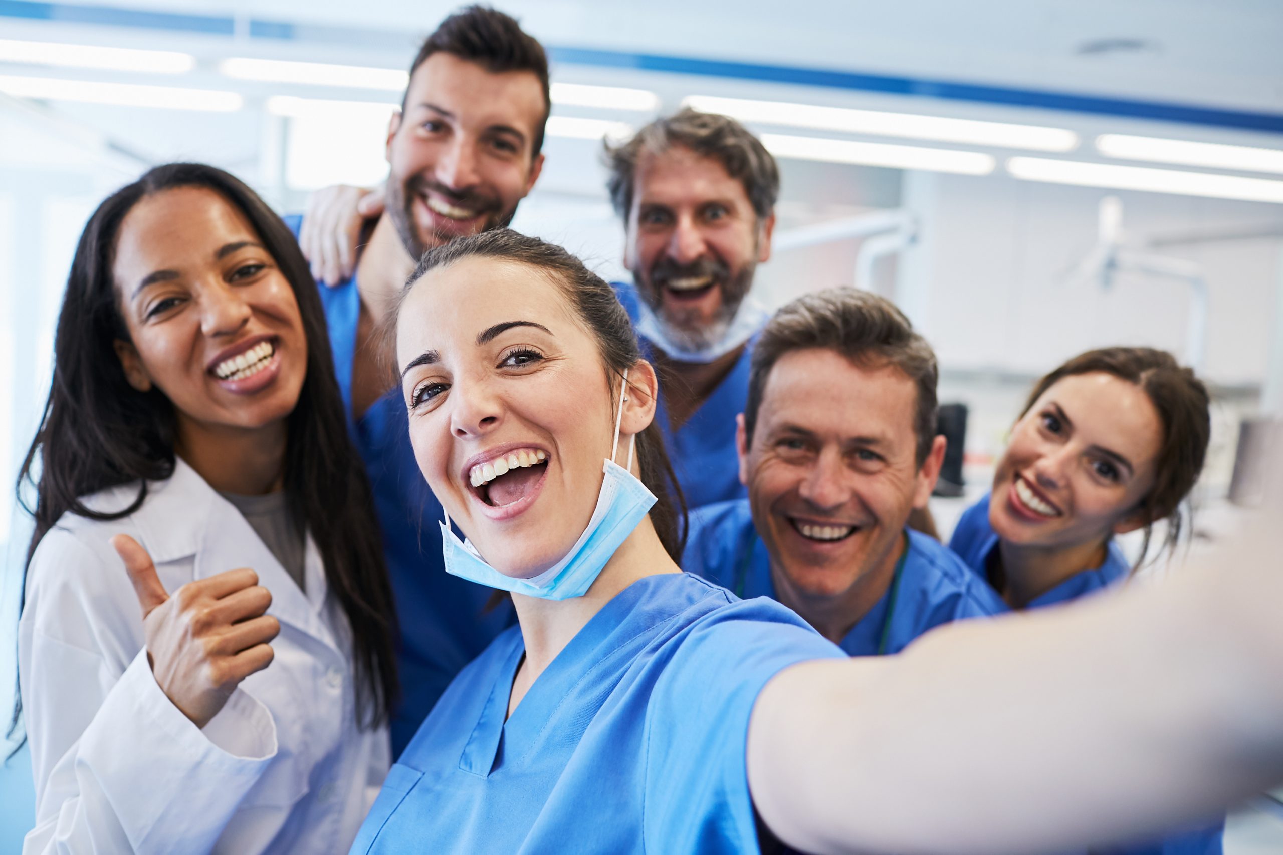 dental healthcare team selfie, woman with brown hair holding the camera to take picture of two other female and five male colleagues, all smiling